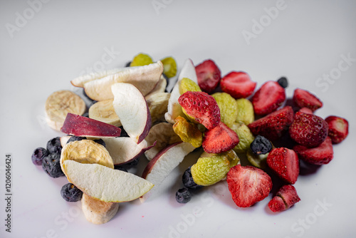 Fototapeta Naklejka Na Ścianę i Meble -  A colorful assortment of freeze-dried apples, bananas, strawberries, and blueberries displayed on a white surface. The vibrant textures and natural colors emphasize their preserved freshness.