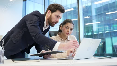 Male manager advises subordinate female worker using laptop in business office. Boss consults talking to employee at workplace. Executive explains work issue. Businessman discussing with colleague