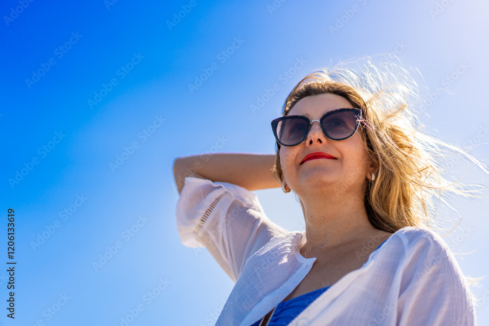 Portrait of beautiful smiling middle-aged woman in sunglasses against blue sky background Portrait of beautiful smiling middle-aged woman in sunglasses against blue sky background
