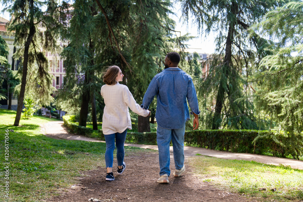 Multiethnic couple holding hands while walking through a park, soaking up the sun and enjoying each other's company on a beautiful day Multiethnic couple holding hands while walking through a park, soaking up the sun and enjoying each other's company on a beautiful day