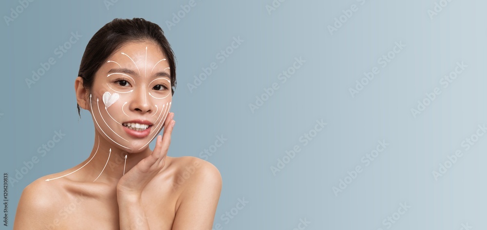 Obraz premium Asian woman enjoys her skincare routine while applying facial cream. She's smiling and appears relaxed, showcasing her commitment to beauty and self-care in a minimalist setting.