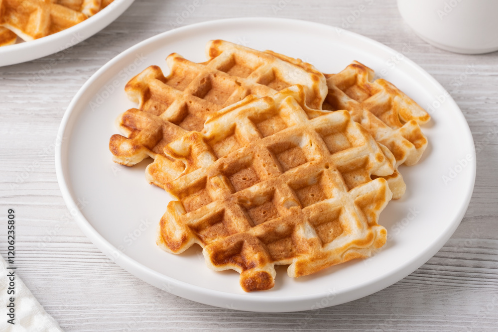 Crispy golden waffles served on a round white plate in a cozy kitchen setting Crispy golden waffles served on a round white plate in a cozy kitchen setting