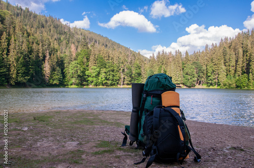 Two backpacks rest on the shore of the picturesque Lake Synevyr in the Carpathian Mountains of Ukraine. The image captures the essence of a summer hiking adventure, with the tranquil lake photo