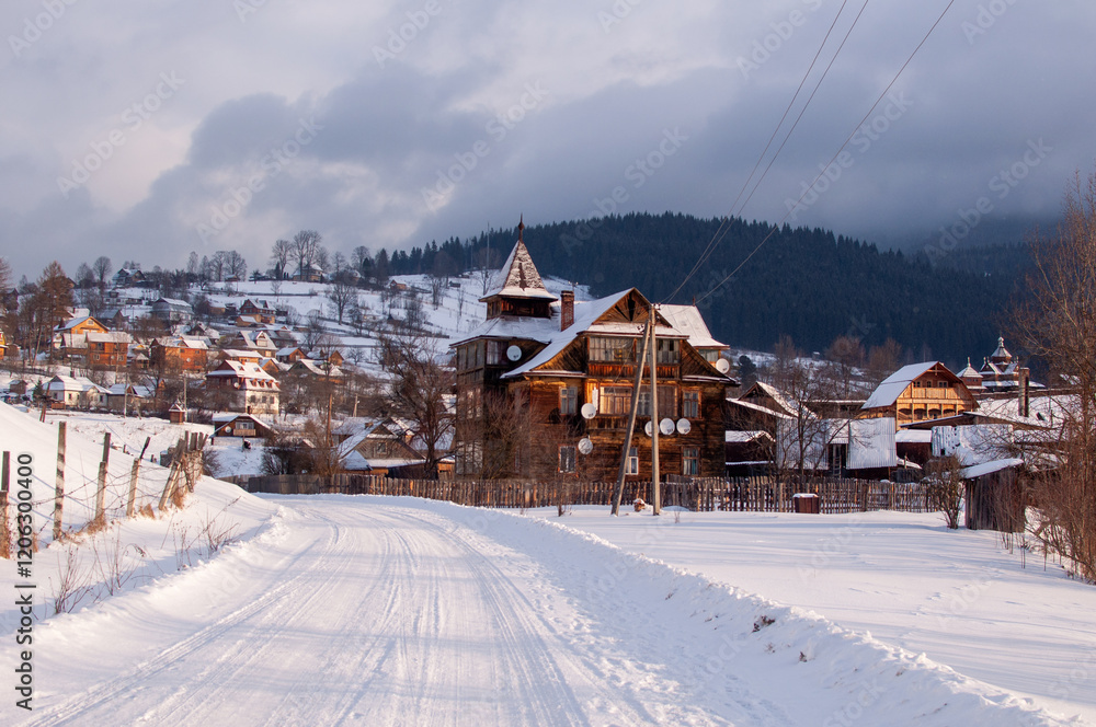 Fototapeta premium A picturesque winter scene in the Ukrainian Carpathian Mountains featuring a snow-covered village with traditional wooden houses. The image captures the serene beauty of a winter landscape