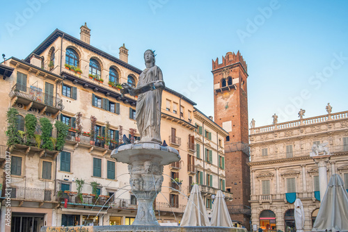 Italian square with fountain and Lamberti clock tower and classic architecture with ancient buildings in Verona, Veneto, Italy. Piazza delle Erbe with Fontana di Madonna. Tourist destination