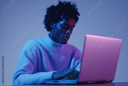 Young man using laptop under vibrant blue and purple lighting. photo