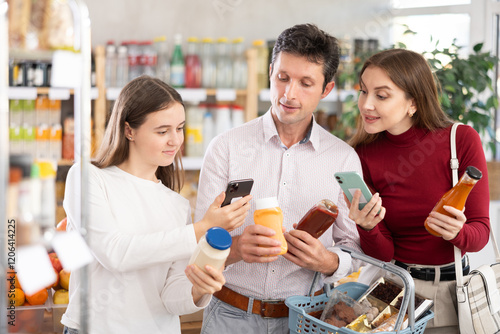 Attentive family with teenage girl scanning QR on bottles of sauce in grocery store photo