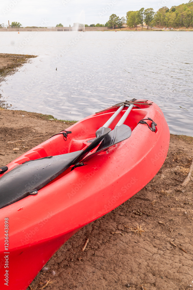 A RED KAYAK ON THE SHORES OF A LAGOON ON A CLOUDY DAY A RED KAYAK ON THE SHORES OF A LAGOON ON A CLOUDY DAY