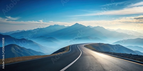 Asphalt road curves along a mountain ridge offering scenic views of distant hazy peaks under a vibrant sky
