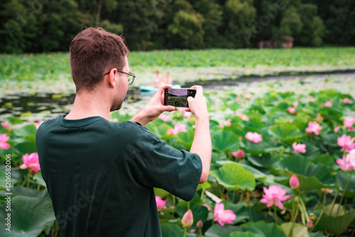Quadro su tela A Russian man takes a photo of Komarov lotus flowers at a lake in Primorsky Krai, Russian Far East