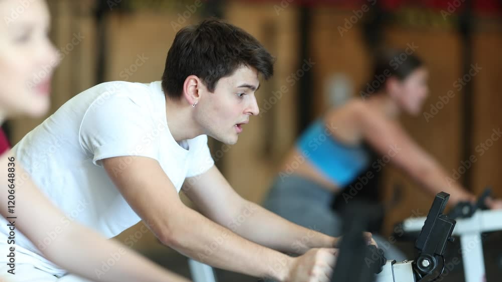 Man on an exercise bike during a group workout to the gym. European in a tracksuit visits a fitness club and works out on a cardio machine. High quality 4k footage