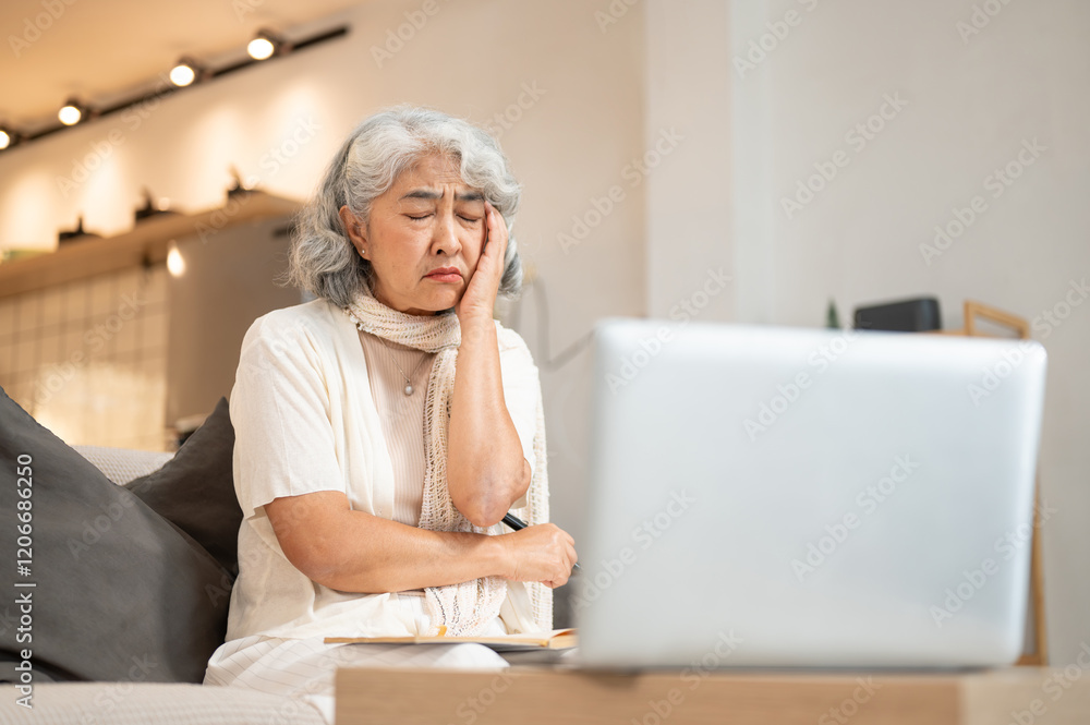 A tired Asian retired woman has a headache while working on her laptop at home. A tired Asian retired woman has a headache while working on her laptop at home.