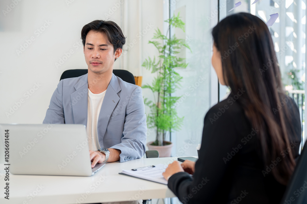 Obraz premium A professional Asian businessman is working on his laptop while interviewing a candidate in office.