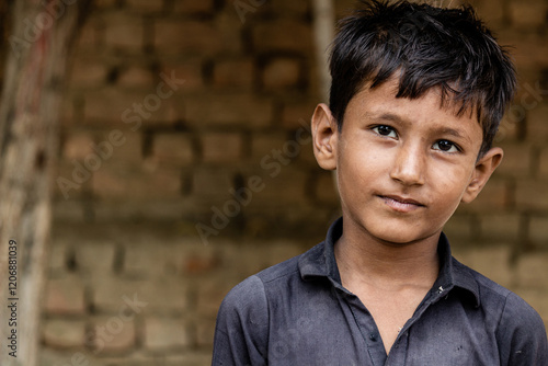 Bild auf Leinwand Portrait of a young boy in traditional clothing with a thoughtful expression, standing against a rustic brick wall in a rural setting