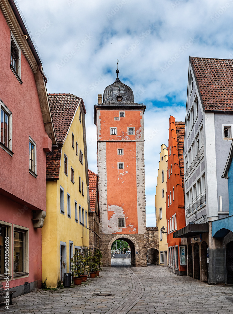 Fototapeta premium Historic Red Brick Tower Surrounded by Trees Under Cloudy Skies in Ochsenfurth, Germany