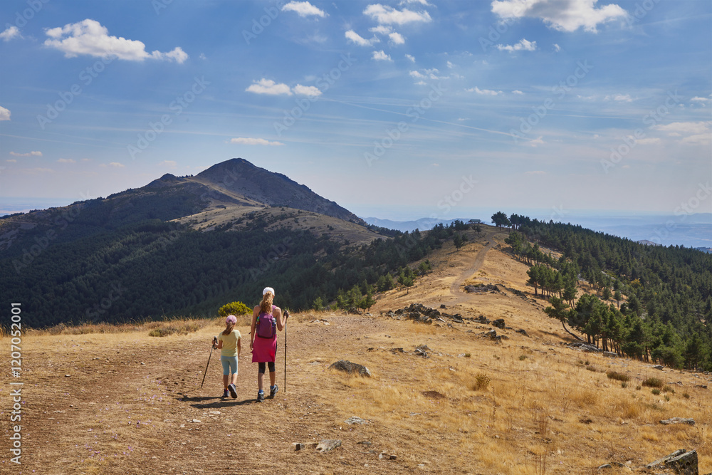 Girl and woman from behind hiking along the mountain ridge towards a peak on the distant horizon, in Madrid, Spain Girl and woman from behind hiking along the mountain ridge towards a peak on the distant horizon, in Madrid, Spain