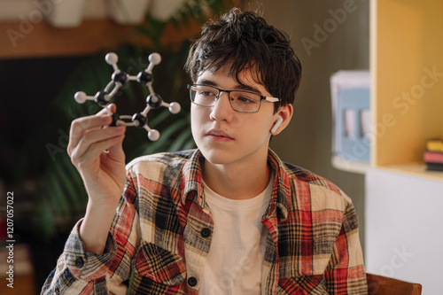 Teenage boy wearing wireless in-ear headphones examining atomic structure at home photo