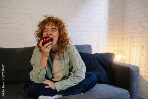 Young woman sitting on sofa and eating apple at home photo