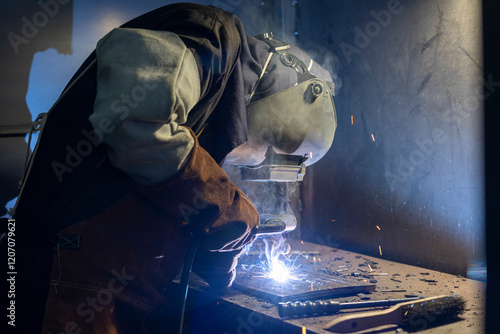 A focused welder in protective gear skillfully creates intricate metalwork, showcasing the art and precision required in welding while illuminating the workspace with sparks. photo