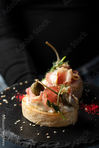 Cuadro en lienzo Bruschetta two pieces with dried meat and sauce on a black plate
