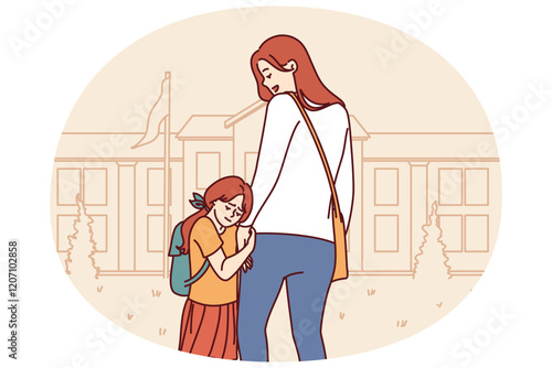 Mom accompanies daughter in elementary school, supporting or motivating girl standing near building of educational institution. Little girl feels attached to mother and does not want to go in school