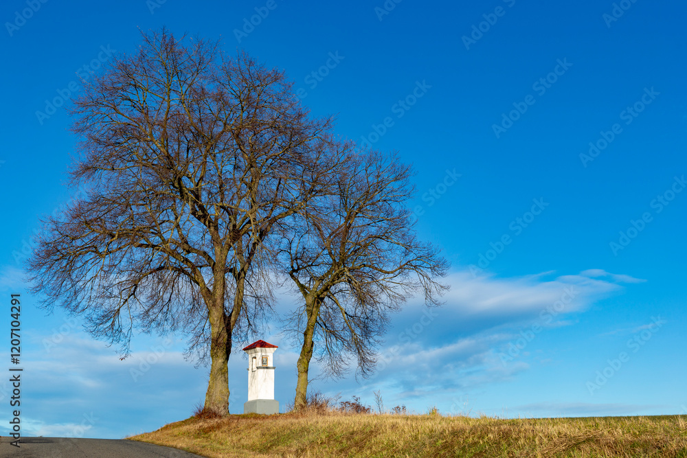 A small chapel on top of a hill with two trees above it. Czechia.