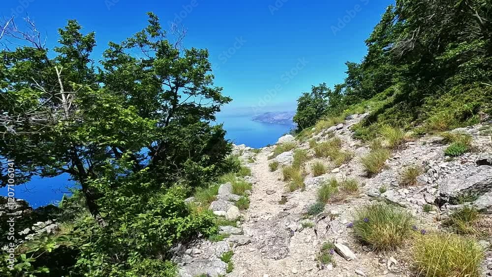 A male hiker walks along a steep mountain trail near the summit of Mount Vosac, Biokovo, Croatia. A male hiker walks along a steep mountain trail near the summit of Mount Vosac, Biokovo, Croatia.