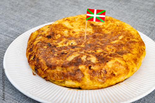 Fototapeta Naklejka Na Ścianę i Meble -  Spanish vegetarian food, portion of homemade tasty potato omelette tortilla de patatas with onion and flag of Basque Country