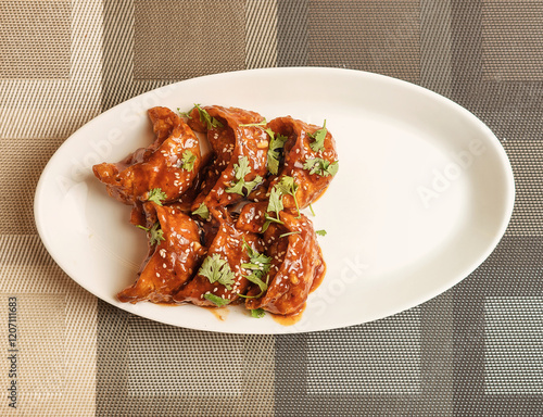 Spicy fried momos coated in flavorful sauce, garnished with sesame seeds and fresh coriander. A delicious Asian street food snack served on a white plate, perfect for restaurant menus and food blogs