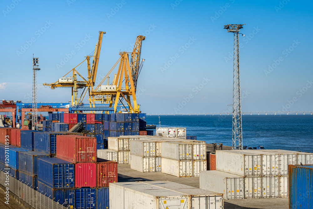 Cargo containers stacked in sea port by Ship-To-Shore cranes on sunny