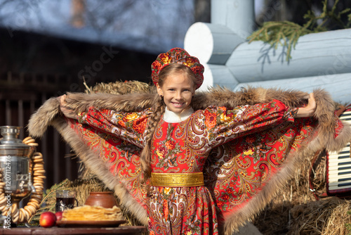 A blonde girl in a national Russian costume on the Maslenitsa holiday. A beautiful russian girl in a national costume made of a fur cape and kokoshnik on the background of a hayloft. 