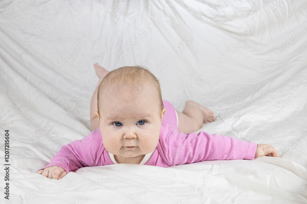 Cute and beautiful 4-month-old baby girl laying on bed and look at the camera. Infant in pink bodysuit on bed against white background. Cute and beautiful 4-month-old baby girl laying on bed and look at the camera. Infant in pink bodysuit on bed against white background.