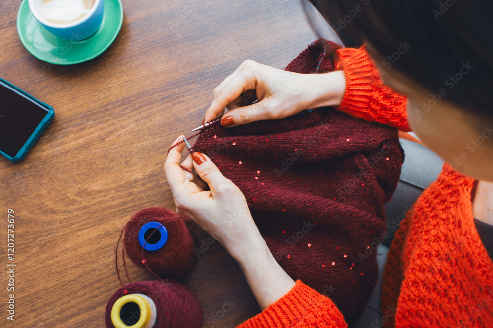 Women hands holding knitting needles and red knitted sweater with sequins. Knitting woman with bobbins of yarn and burgundy knitwear. Sequin pattern in needlework. Knitting hobby. Knitter work.