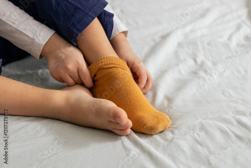 Child taking off yellow socks while sitting on bed, preparing for a restful night's sleep photo