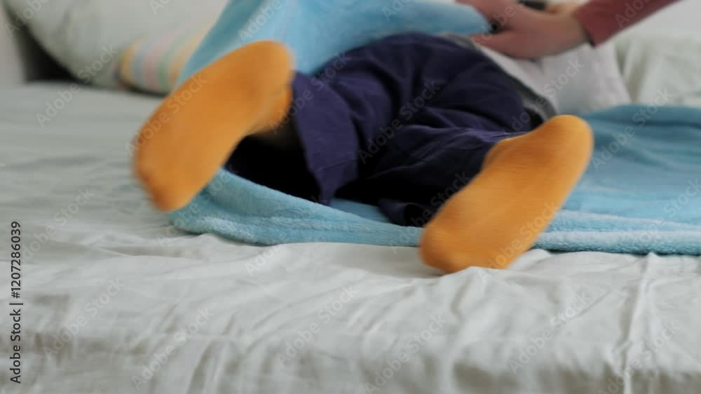 Mother rolling up her child into a soft blue blanket and unrolling him playfully Mother rolling up her child into a soft blue blanket and unrolling him playfully