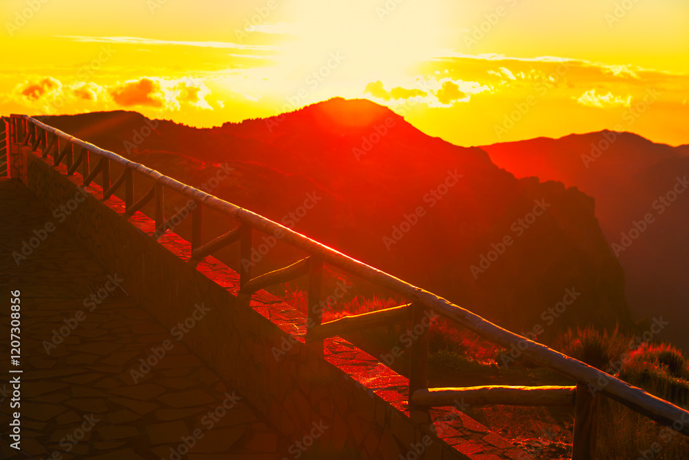 Golden sunset over mountain peaks with a rustic wooden railing in the foreground. Warm light bathes the landscape, creating a serene and breathtaking view of nature's beauty