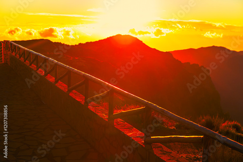 Obraz na płótnie Golden sunset over mountain peaks with a rustic wooden railing in the foreground. Warm light bathes the landscape, creating a serene and breathtaking view of nature's beauty w salonie