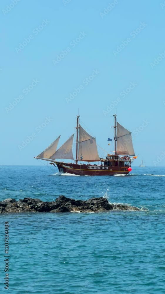 A wooden sailboat with classic design sails gracefully close to a rugged rocky shoreline, showcasing maritime elegance and coastal beauty. Vertical video. A wooden sailboat with classic design sails gracefully close to a rugged rocky shoreline, showcasing maritime elegance and coastal beauty. Vertical video.