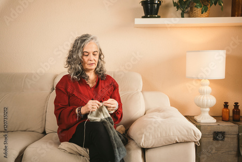 Woman in red sweater knitting on beige sofa at home