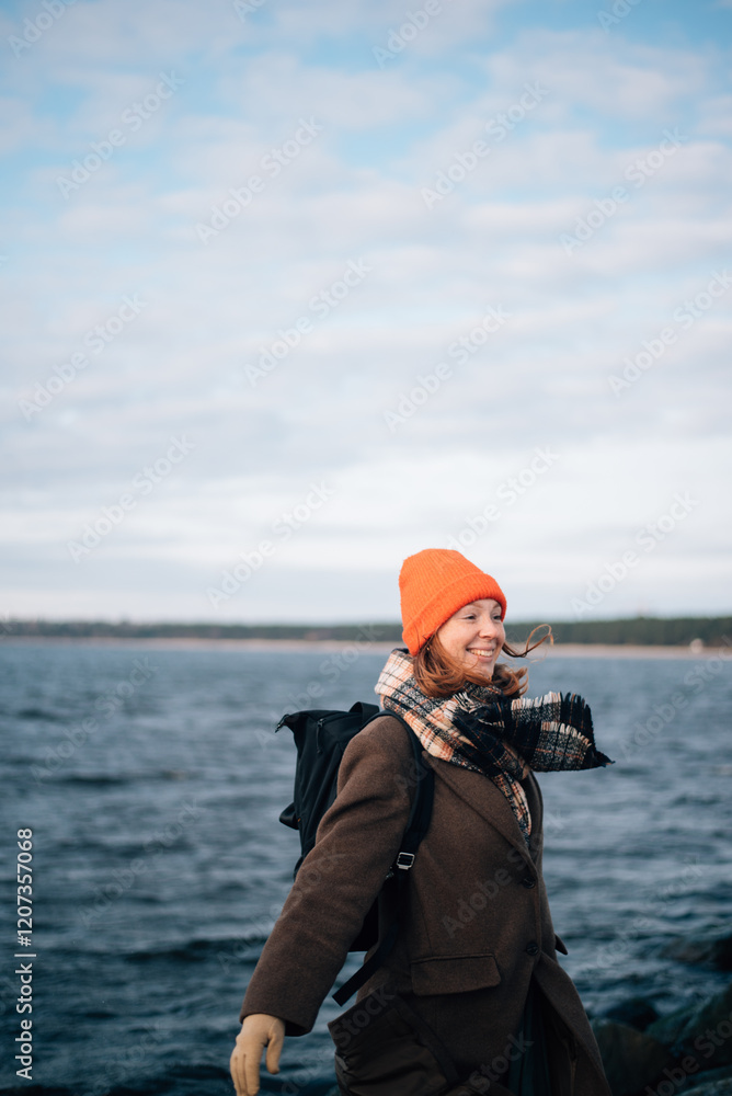 Obraz premium red-haired girl in an orange hat and coat near the sea