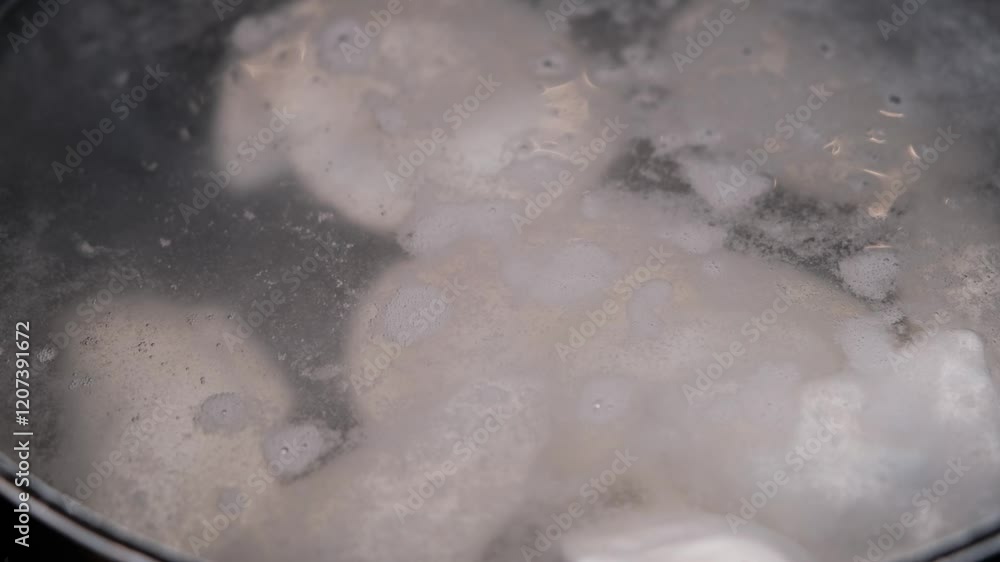 A close-up of hot, steamy water with pierogi resting at the bottom of the pot, visible beneath the bubbling surface A close-up of hot, steamy water with pierogi resting at the bottom of the pot, visible beneath the bubbling surface