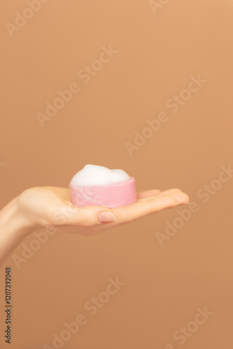 Close-up of female palm of hand with pink solid face cleanser or foamy solid soap. Self care advertising. A clean ready-made template for brand presentation, copy space. Isolated beige background photo
