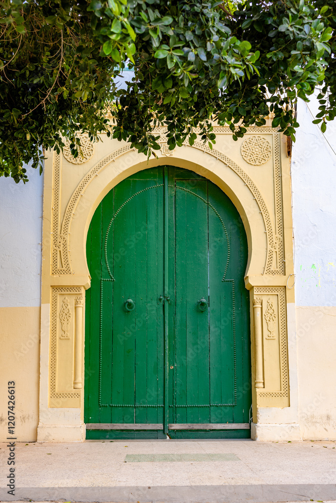 Fototapeta premium Green wooden door in a yellow colored frame of a luxurious house in Tunis, Tunesia