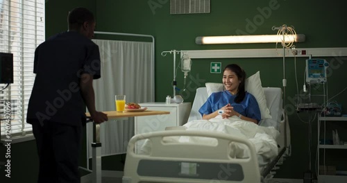 Young woman recovers in a hospital room. An African doctor delivers her breakfast.