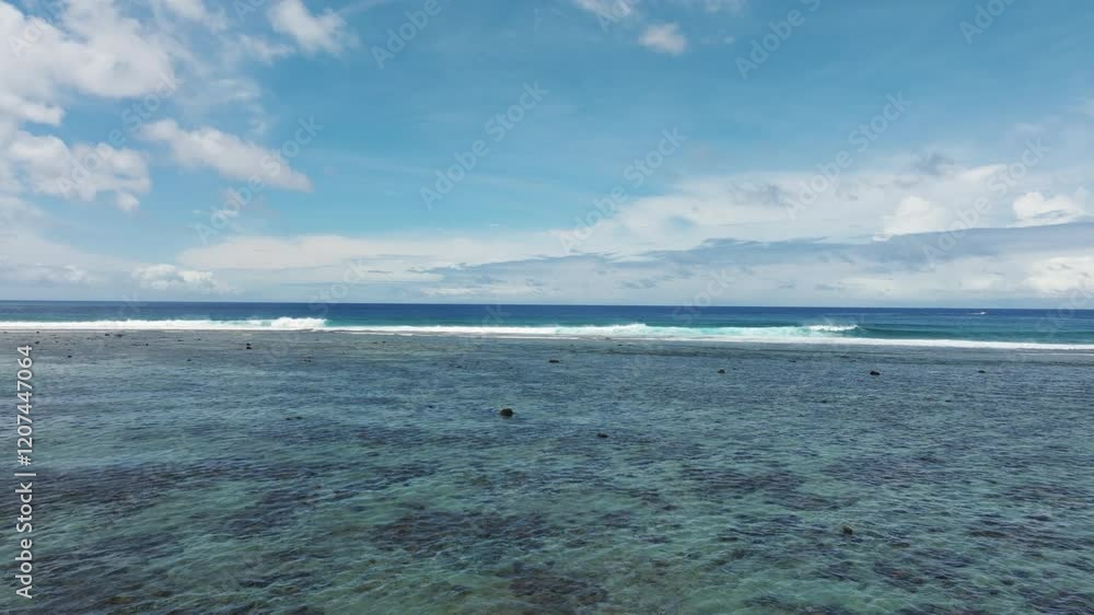Low aerial dolly over fringing coral reef with exposed rocks to open ocean as waves crash and spread foam and spray Low aerial dolly over fringing coral reef with exposed rocks to open ocean as waves crash and spread foam and spray