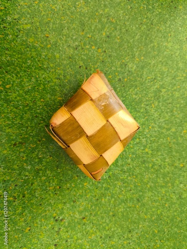 a ketupat wrapped in fragrant pandan leaves on a green plastic table photo