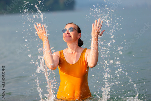 An adult woman splashes sea water on herself. She is wearing a yellow wet T-shirt and sunglasses. photo