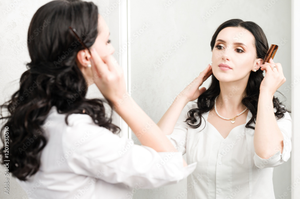 A woman with dark, wavy hair uses a hairbrush to style her locks while looking in a mirror, wearing a white blouse and pearl necklace. A woman with dark, wavy hair uses a hairbrush to style her locks while looking in a mirror, wearing a white blouse and pearl necklace.