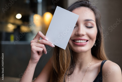 Smiling woman with her eyes closed holding a blank card in front of her face