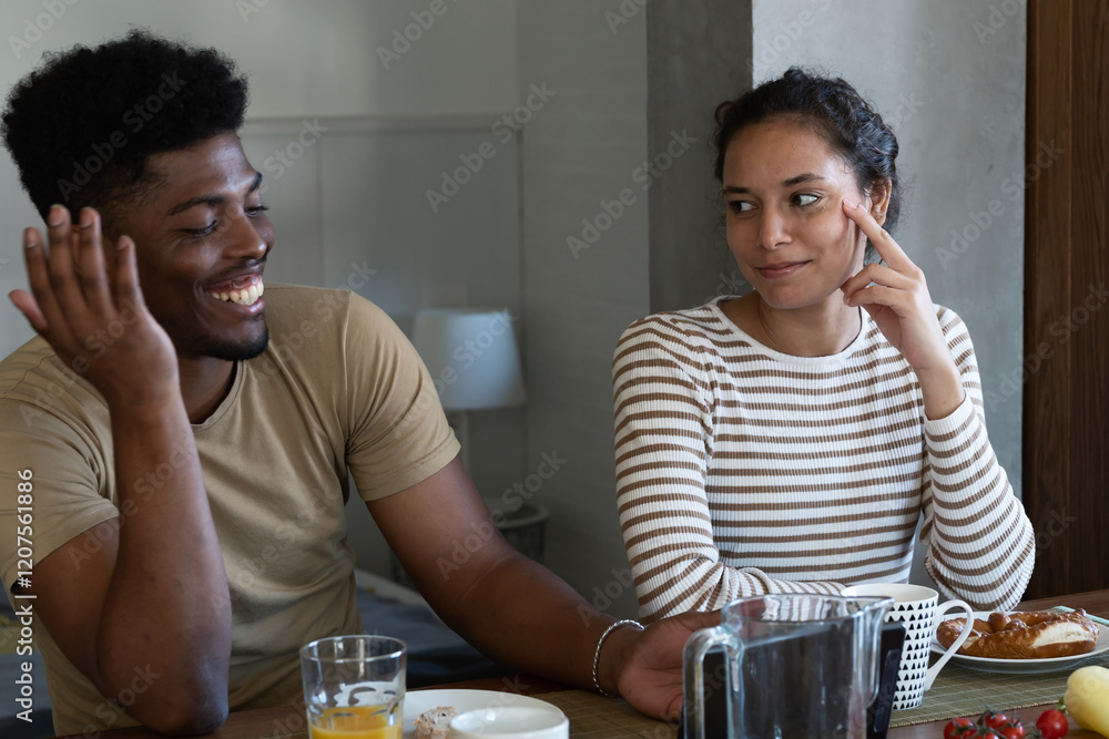 A young couple shares a lighthearted conversation at the breakfast table, smiling and enjoying each other's company during a relaxed morning at home A young couple shares a lighthearted conversation at the breakfast table, smiling and enjoying each other's company during a relaxed morning at home